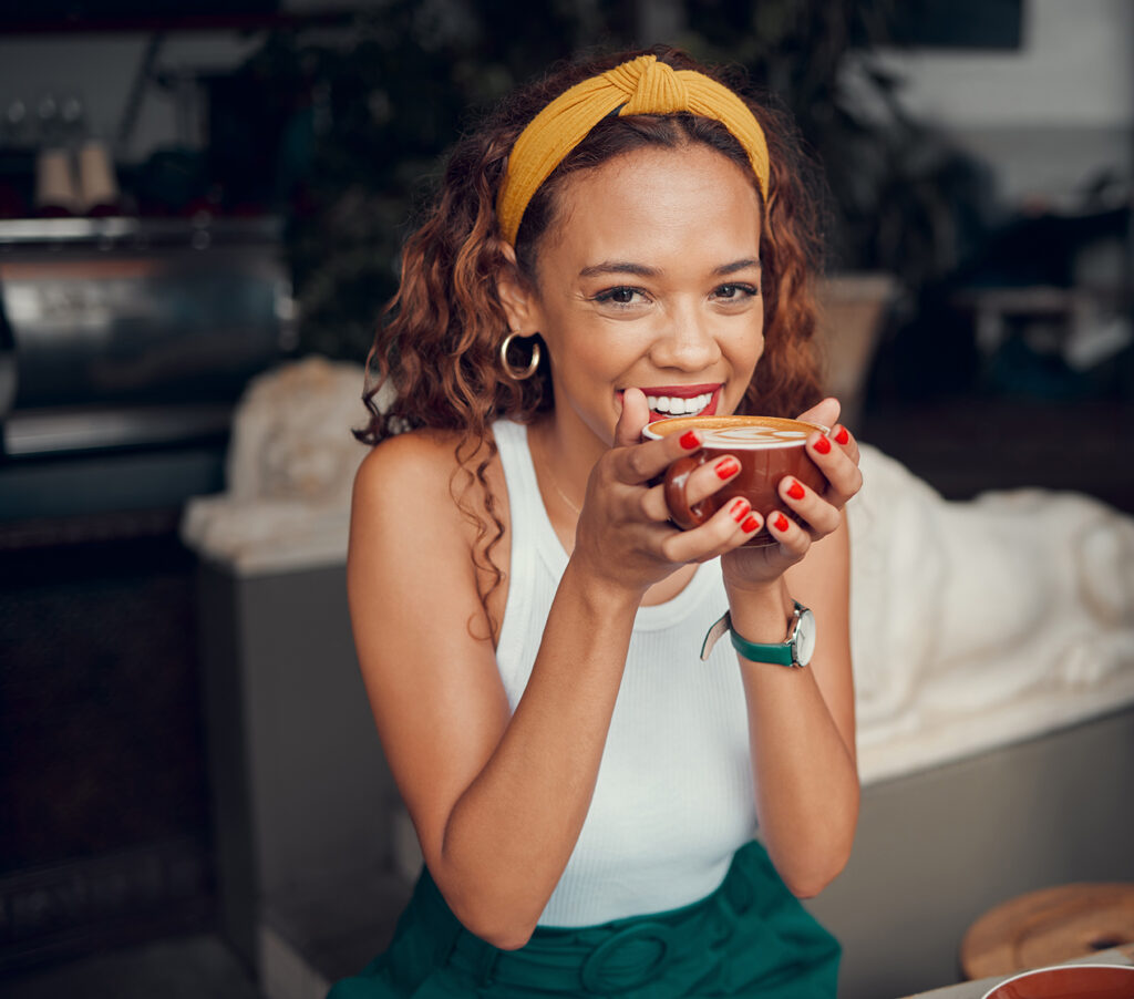 Smile, happy and coffee shop young woman enjoying a cup of tea in a restaurant or cafe on her lunch break. Portrait of happy customer drinking her morning caffeine or cappuccino with happiness
